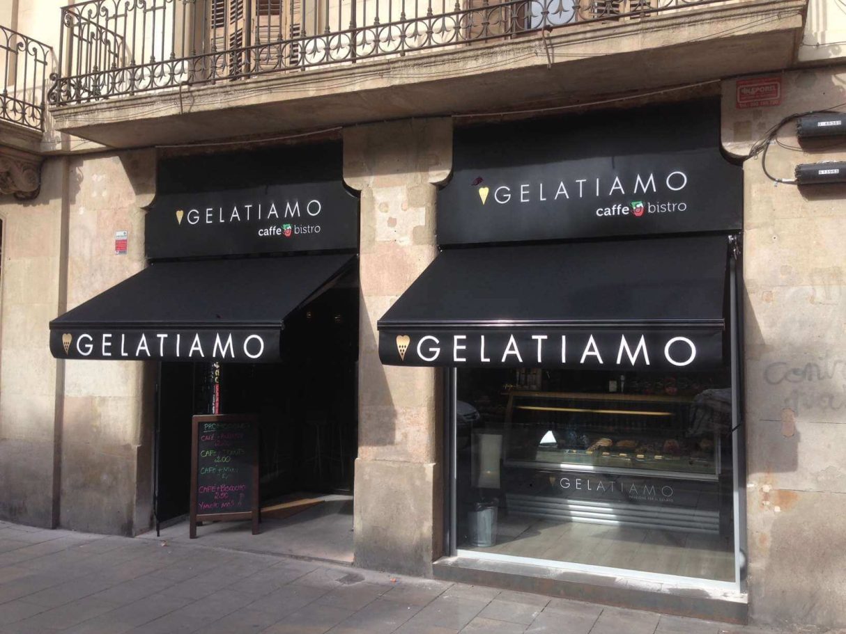 Fachada de una heladería con toldos negros y el nombre "Gelatiamo".