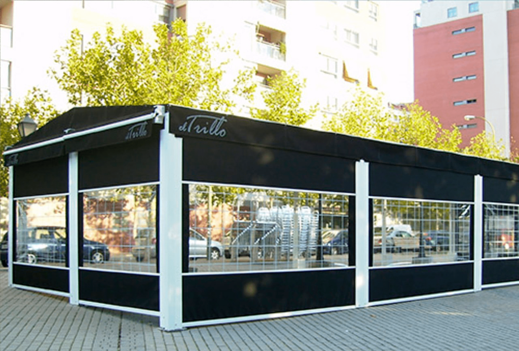 Tienda grande con estructura negra y paneles de vidrio, ubicada en una plaza urbana.