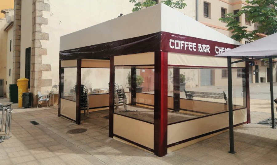 Tienda efímera con estructura de metal y paneles de vidrio, ubicada en una calle.